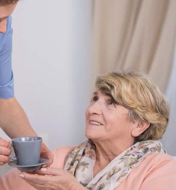 Carer bringing a cup of tea to a smiling older lady
